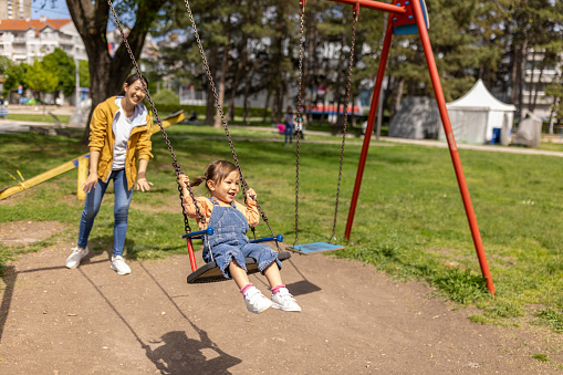 Mother swinging her daughters in a public park