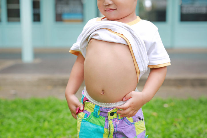 Close up happy little boy lifting his shirt show exposing his big tummy.
