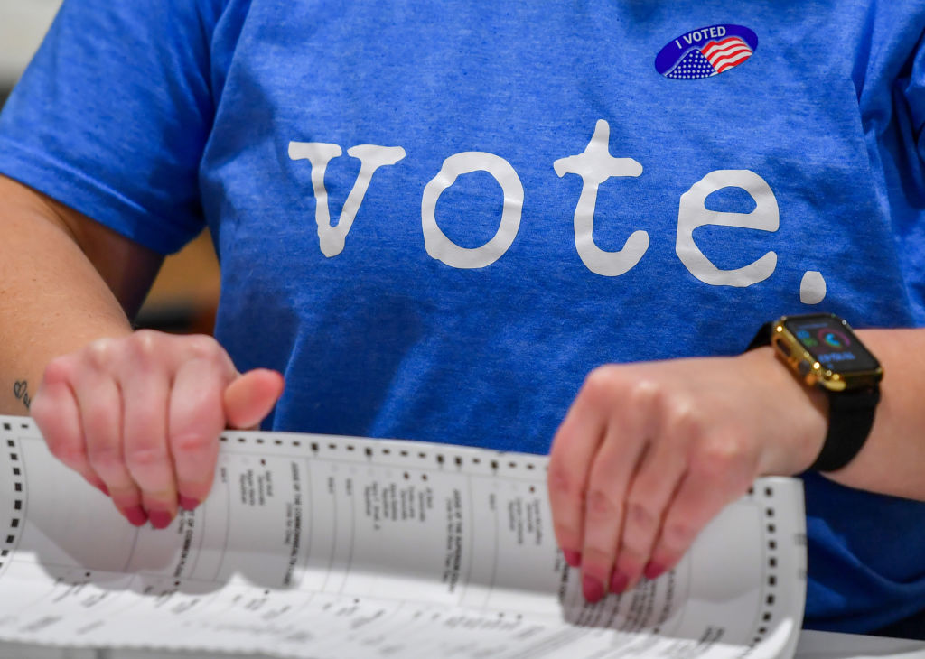 A woman wearing a Vote t-shirt prepares mail-in ballots to...