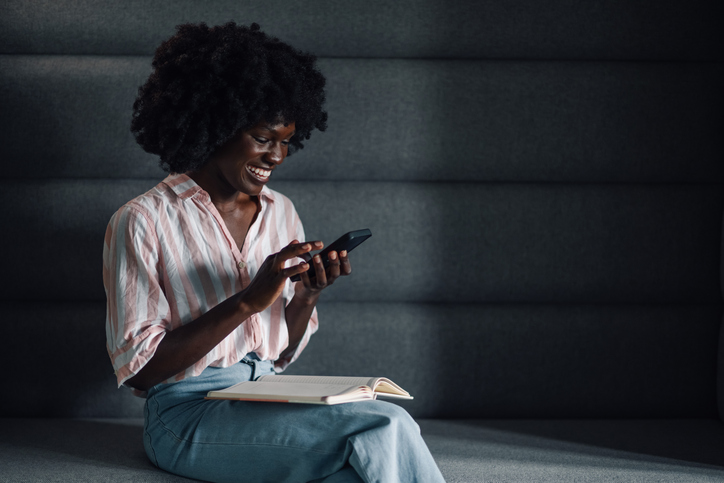 Interracial casual manager with textbook reading messages on a phone.