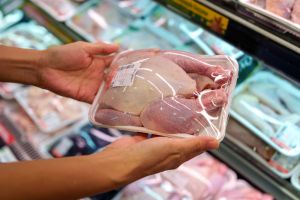 A cropped shot of a woman selecting raw chicken meat at a grocery store