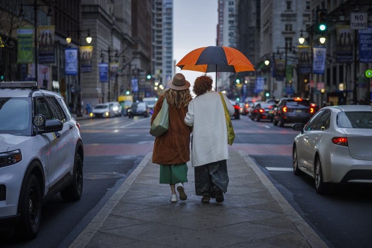 Urban exploration in rainy weather. Middle-aged friends walking downtown Philadelphia streets during spring drizzle.