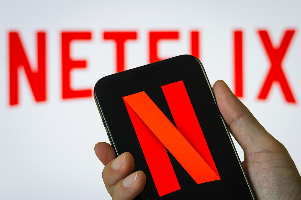 Hand Holding Smartphone Displaying Netflix (NFLX) Logo with Background Branding