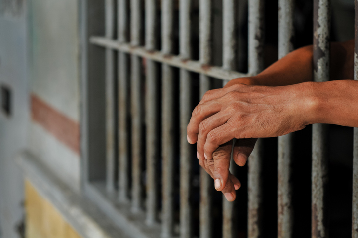 prisoner's hands behind bars with black background